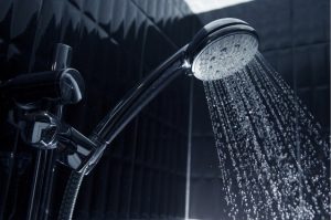 Water flowing from shower head in black tiled shower.